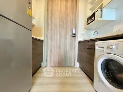 Modern kitchen with washing machine and microwave, featuring sleek wooden cabinets and light wood flooring.