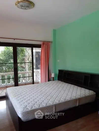 Spacious bedroom with large window and balcony access, featuring a comfortable bed and vibrant wall color.