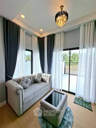 Elegant living room with plush sofa, chandelier, and large windows offering natural light.