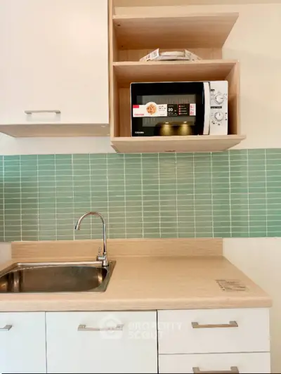 Modern kitchen with sleek cabinetry and microwave, featuring stylish green tile backsplash.