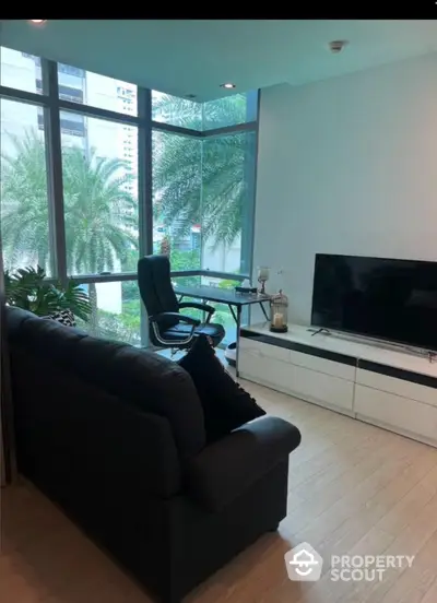 Modern living room with large windows and garden view, featuring a sleek TV setup and comfortable seating.