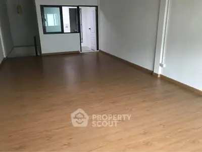 Spacious empty room with wooden flooring and large window, perfect for customization.