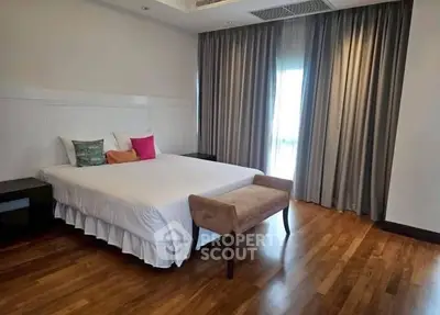 Spacious bedroom with elegant wooden flooring and large window draped with curtains.