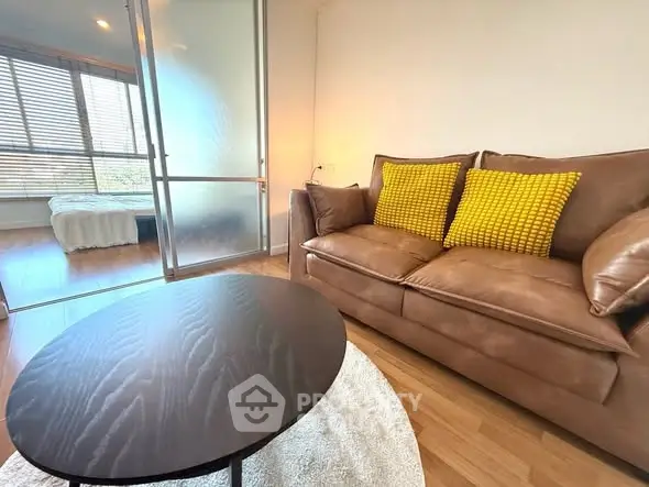 Modern living room with brown leather sofa and yellow cushions, adjacent to a cozy bedroom.