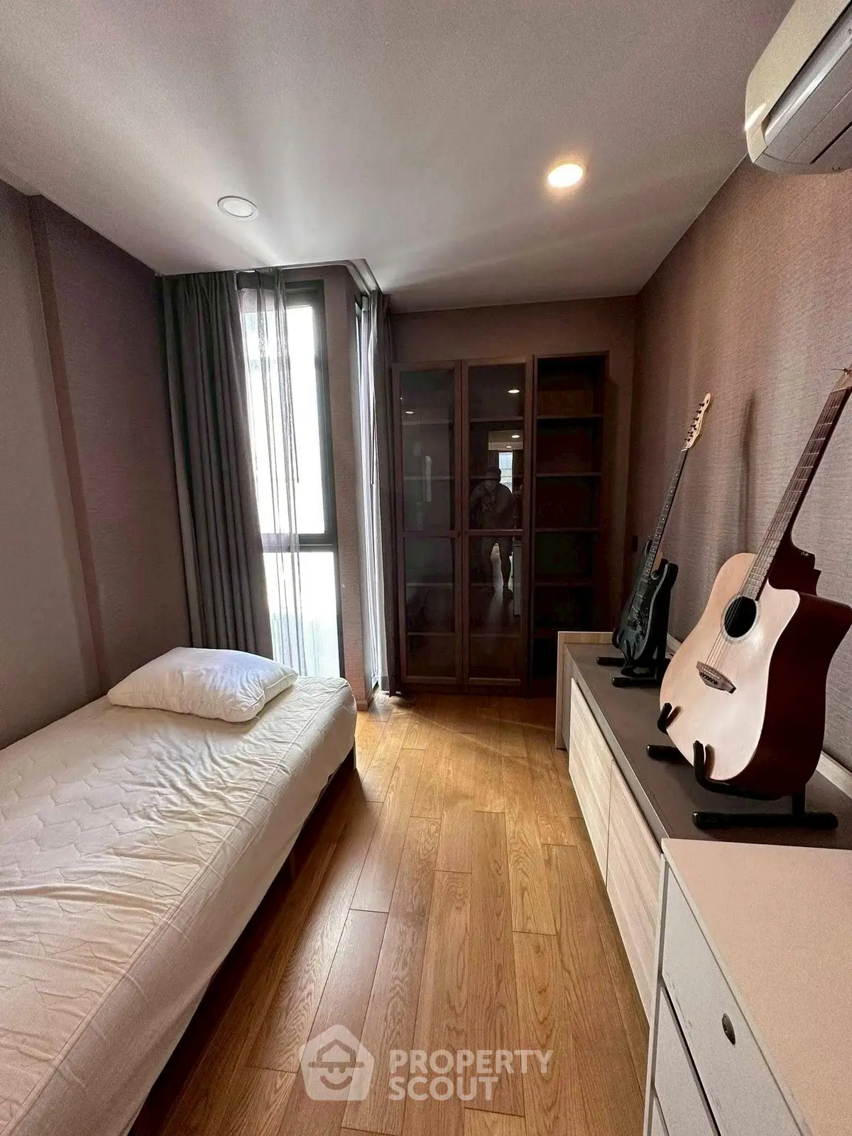 Cozy bedroom with wooden flooring and guitars, perfect for music lovers.