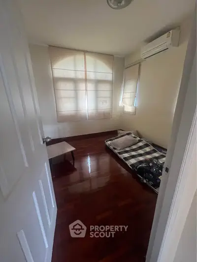 Cozy bedroom with wooden flooring and natural light, featuring a minimalist setup and air conditioning.