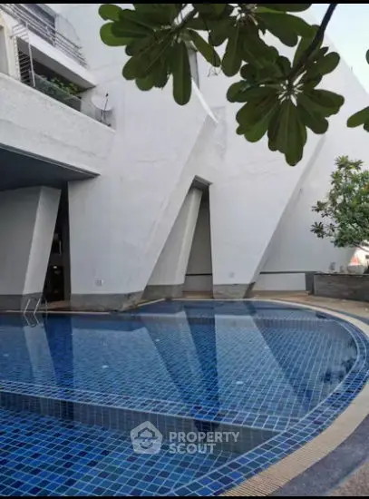 Luxurious modern building with a stunning blue-tiled pool and lush greenery.