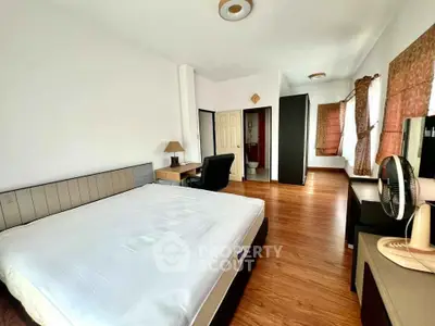 Spacious bedroom with modern furnishings and wooden flooring, featuring a comfortable bed and ample natural light.