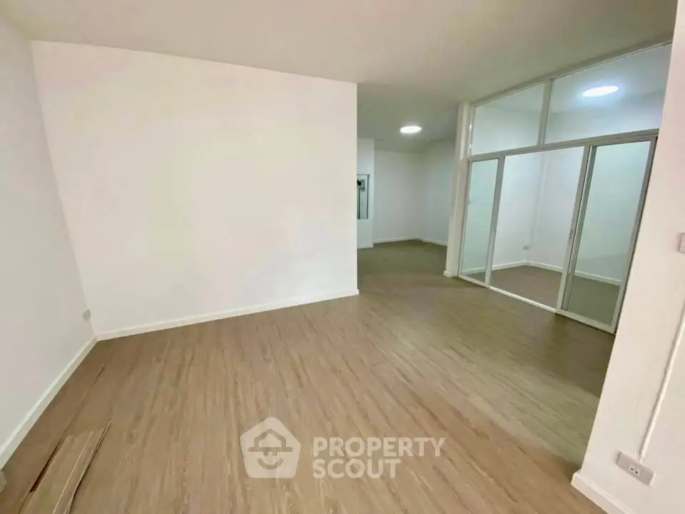 Spacious empty room with wooden flooring and glass partition, ideal for customization.
