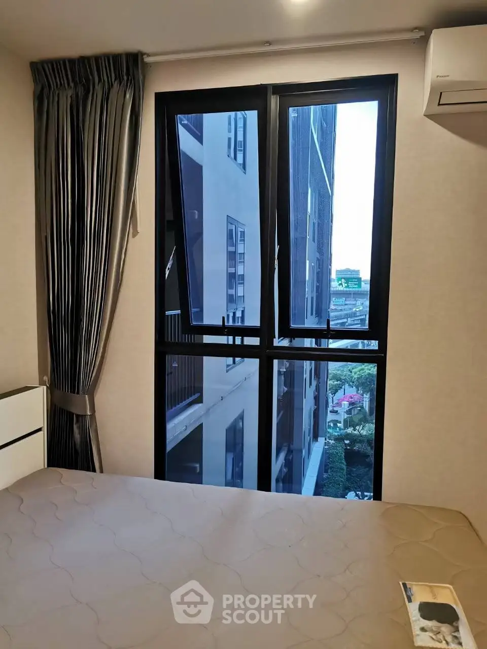 Modern bedroom with large window offering urban view, featuring elegant curtains and air conditioning.