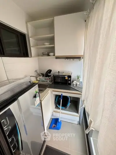 Compact kitchen with modern appliances and open shelving in cozy apartment.