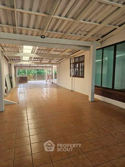 Spacious covered terrace with tiled flooring and large windows, ideal for outdoor gatherings.