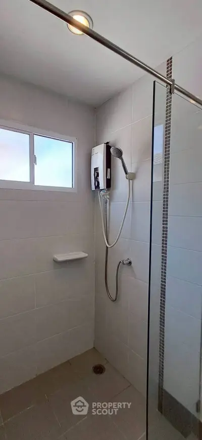 Modern bathroom shower area with glass partition and electric water heater.