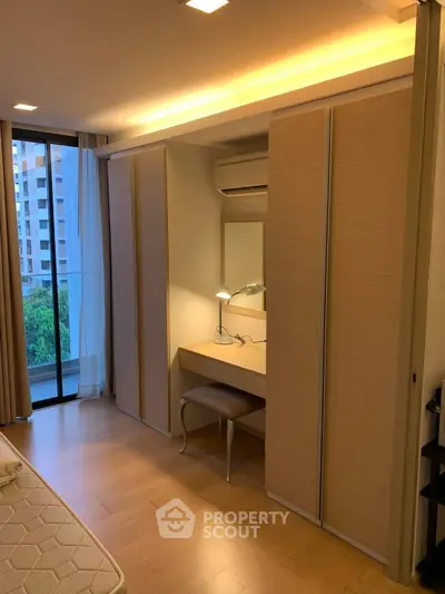 Modern bedroom with built-in wardrobe and vanity, featuring a large window with city view.