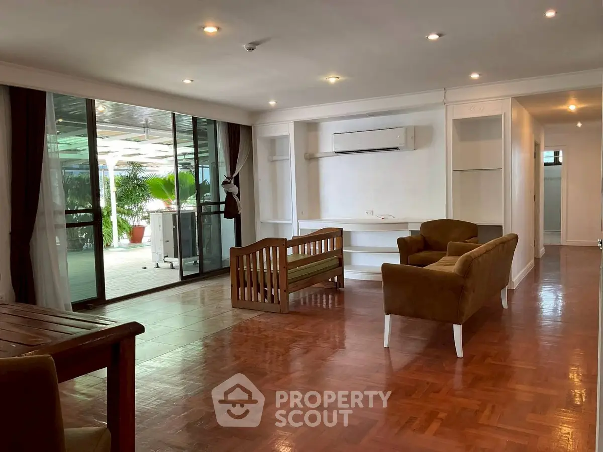 Spacious living room with elegant wooden flooring and large glass doors opening to a balcony.