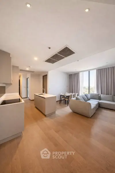 Spacious modern living room with open kitchen and large windows offering natural light.