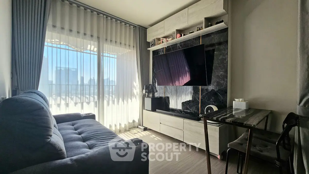 Modern living room with large TV, stylish sofa, and city view through sheer curtains.