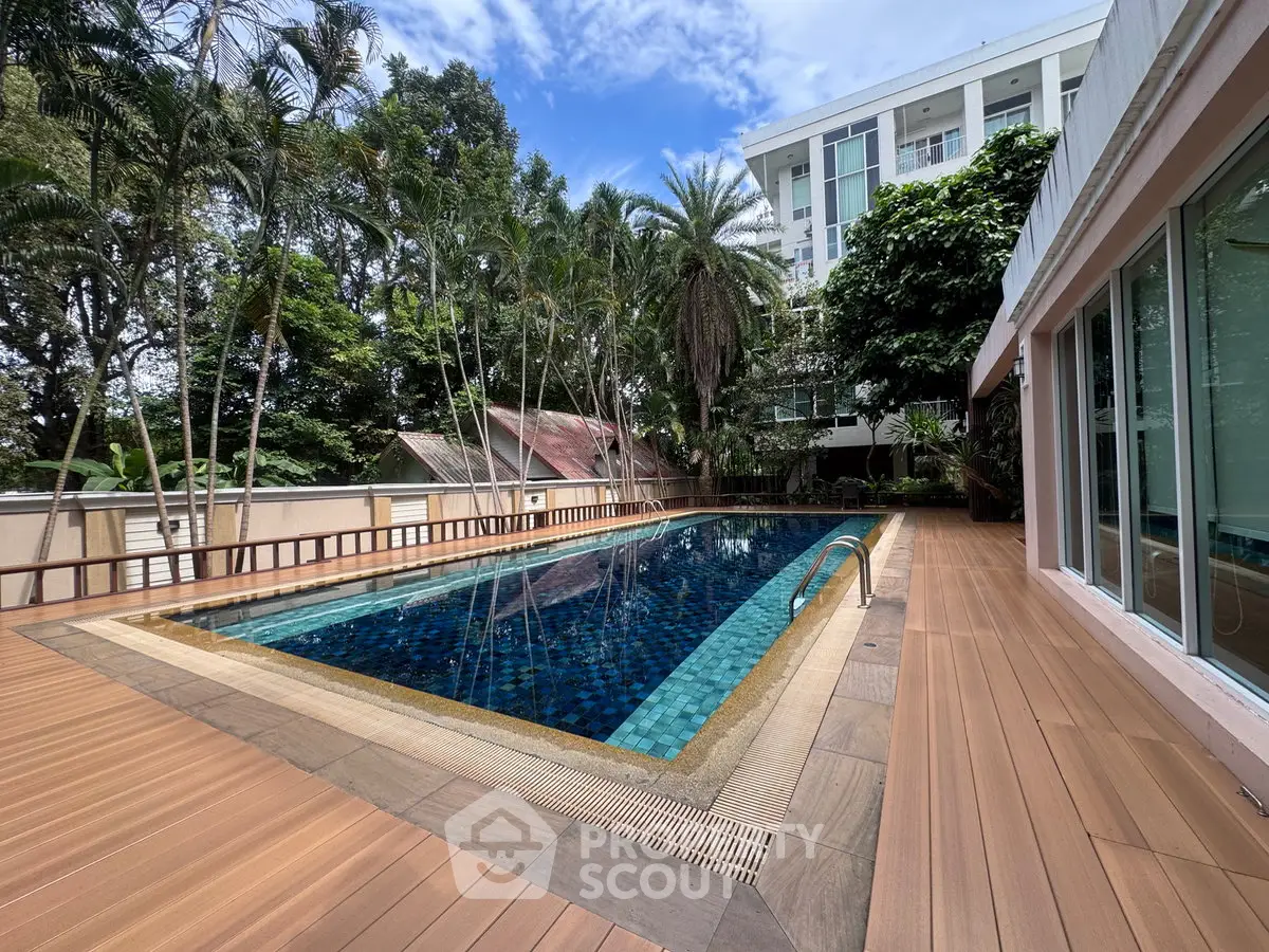 Luxurious outdoor pool area with lush greenery and modern building backdrop, perfect for relaxation and leisure.