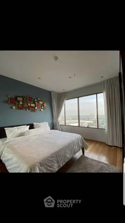Luxurious bedroom with large window offering stunning city views, elegant decor, and cozy ambiance.