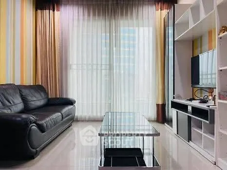 Modern living room with sleek black leather sofa and glass coffee table, featuring floor-to-ceiling windows.