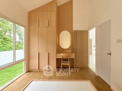 Modern bedroom with wooden flooring, built-in wardrobe, and large window overlooking greenery.