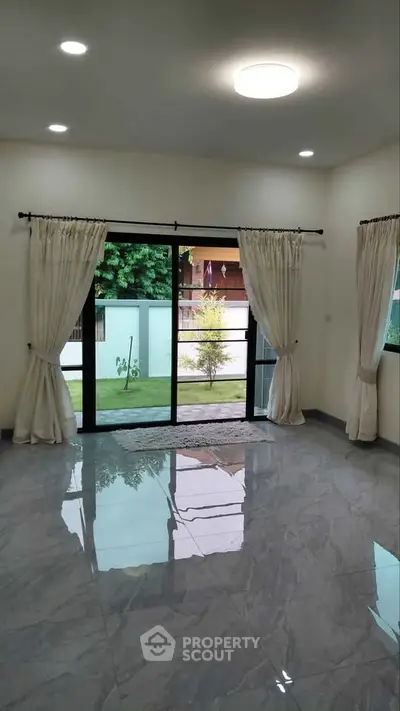 Spacious living room with large windows and garden view, featuring elegant curtains and glossy tiled floor.