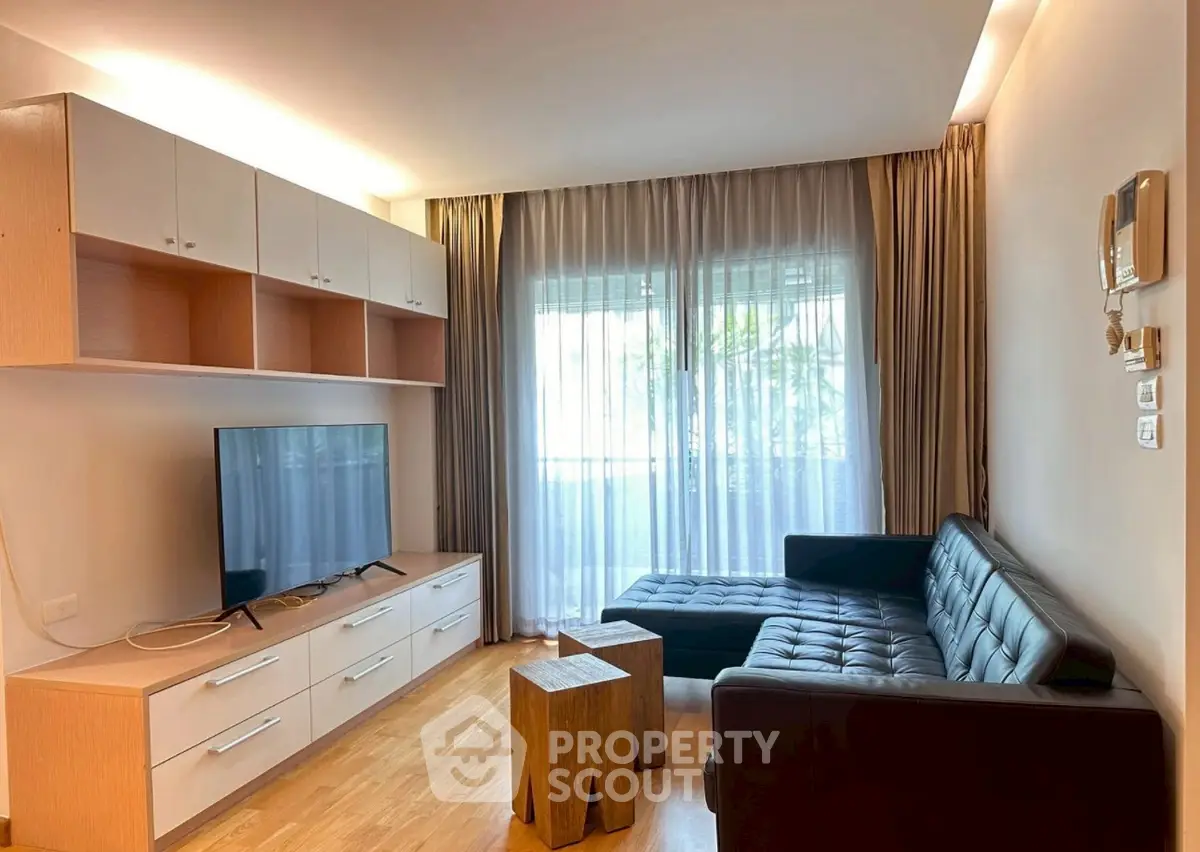 Modern living room with sleek furniture and natural light, featuring a large TV and stylish decor.