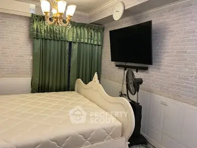 Charming bedroom with elegant chandelier and wall-mounted TV, featuring classic white bed and green curtains.