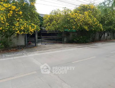 Charming residential entrance with lush yellow flowering trees and secure gate