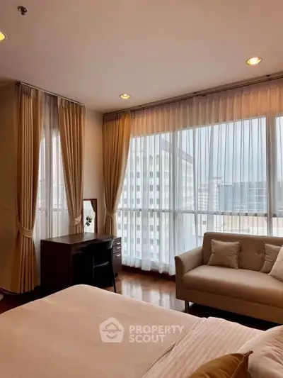 Elegant bedroom with large windows and city view, featuring cozy sofa and desk.