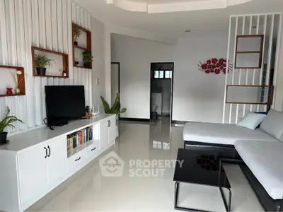 Modern living room with sleek white furniture and stylish decor, featuring a large sectional sofa and flat-screen TV.