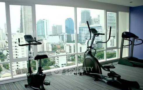 Modern gym with city view in high-rise building, featuring exercise equipment and large windows.