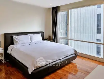 Spacious bedroom with large window and modern furnishings in a luxury apartment.