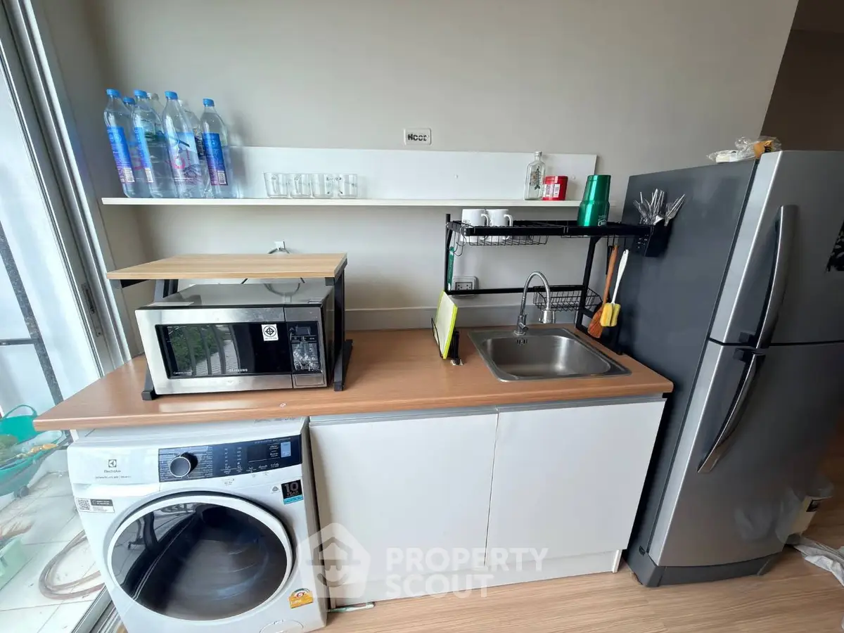 Modern kitchen with washing machine, microwave, and fridge in compact layout.
