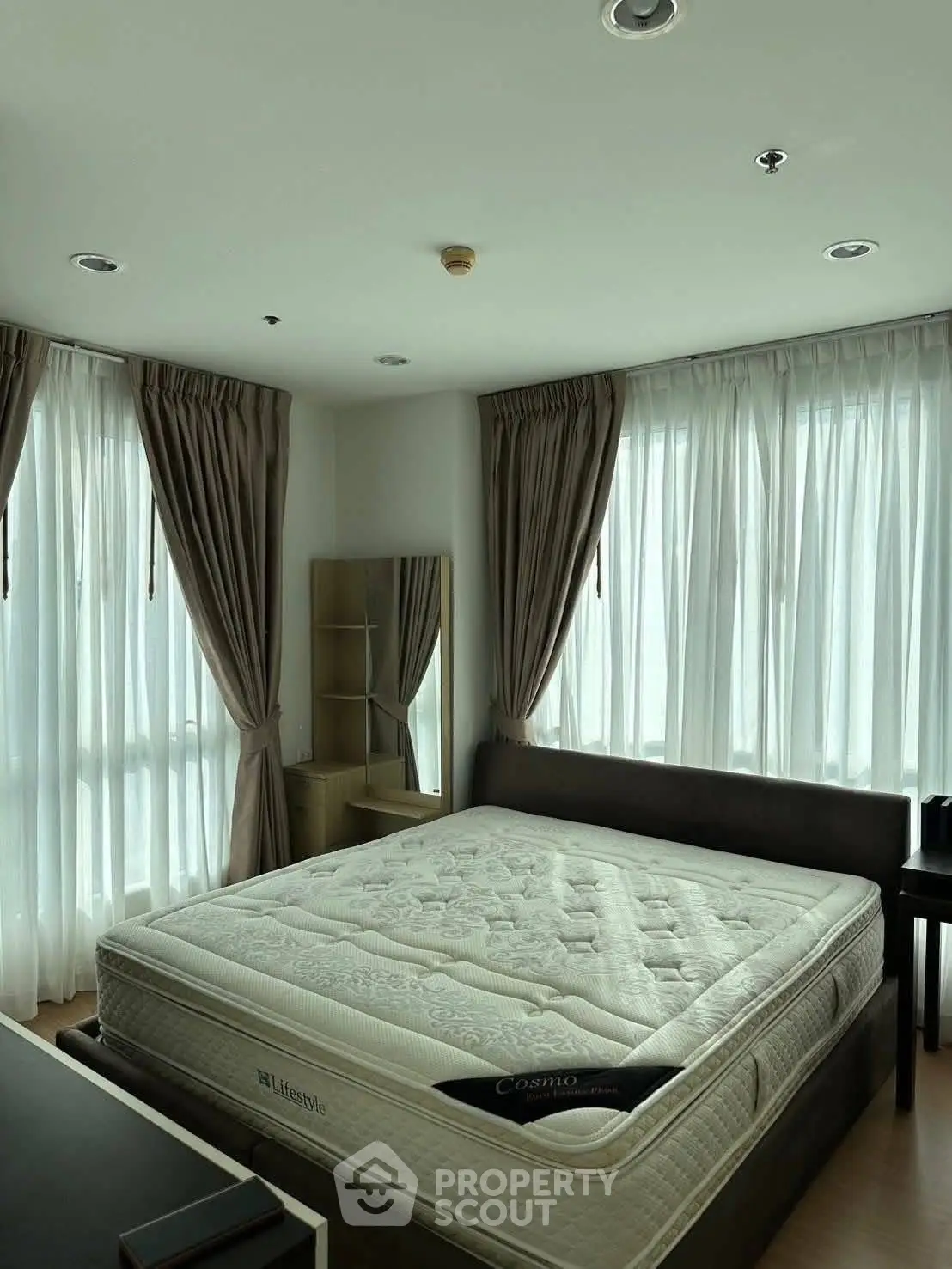 Spacious bedroom with large windows and elegant curtains, featuring a comfortable bed and modern decor.