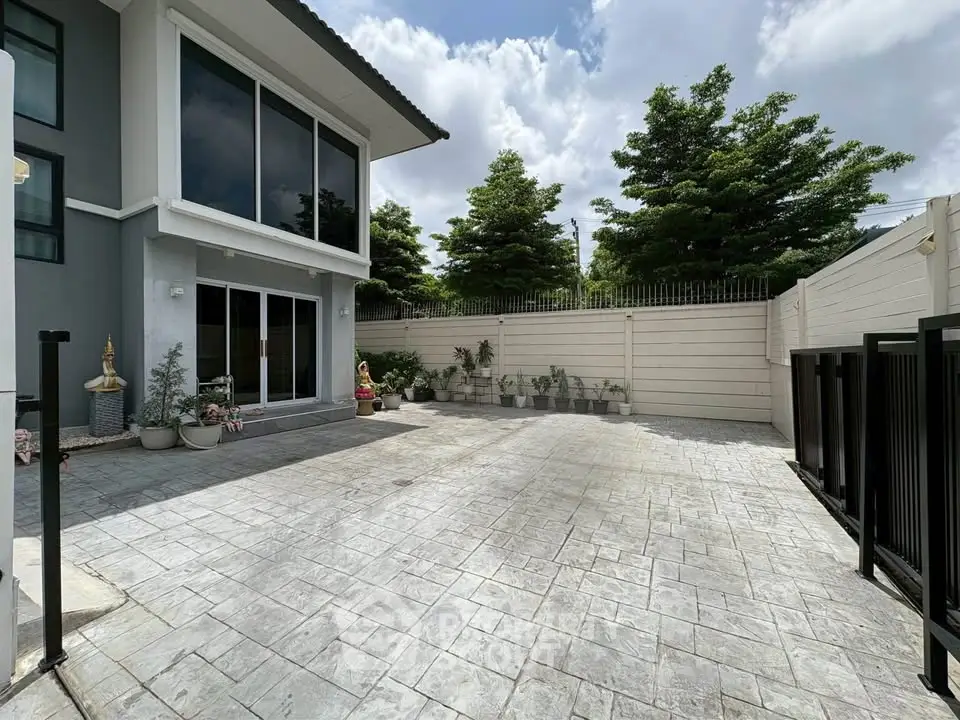 Spacious modern home exterior with large paved patio and lush greenery.