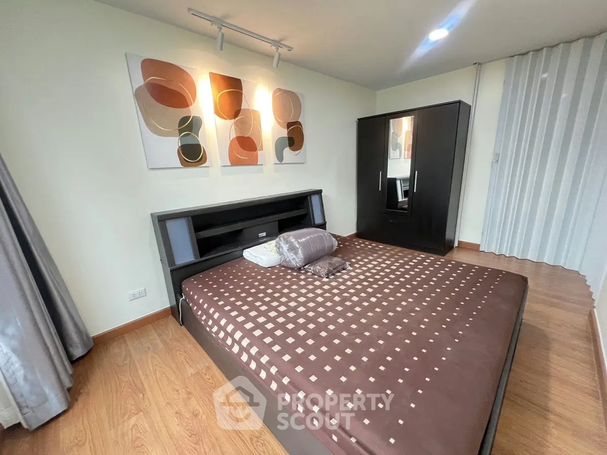 Modern bedroom with stylish decor and wooden flooring, featuring a sleek wardrobe and contemporary artwork.