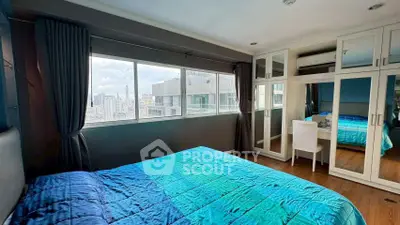 Spacious bedroom with city view and modern furnishings in high-rise apartment.