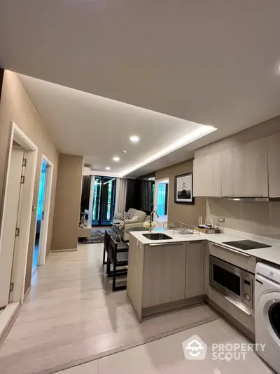 Modern kitchen with open layout flows into a spacious living area, featuring built-in appliances, sleek cabinetry, and contemporary lighting.