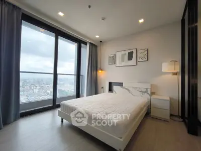 Modern bedroom with large windows offering stunning city views, featuring elegant decor and ample natural light.