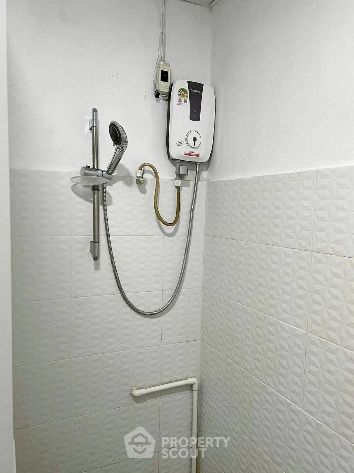 Compact bathroom with electric shower heater and tiled walls, ideal for efficient space use.