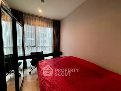 Cozy bedroom with red bedding and large window offering natural light in modern apartment.