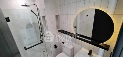 Modern bathroom with sleek shower and round mirror in stylish real estate property.