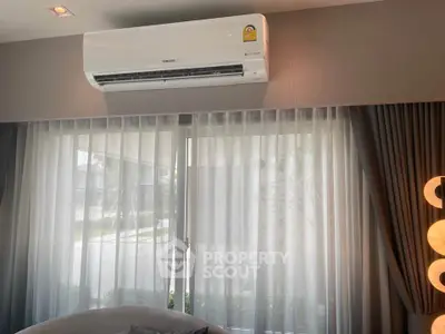 Modern living room with air conditioning and large window draped with sheer curtains.