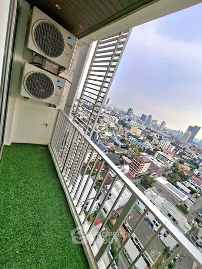 Stunning city view from a high-rise balcony with artificial grass flooring and air conditioning units.