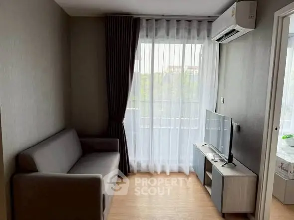 Cozy living room with modern sofa and TV, featuring large window with curtains.