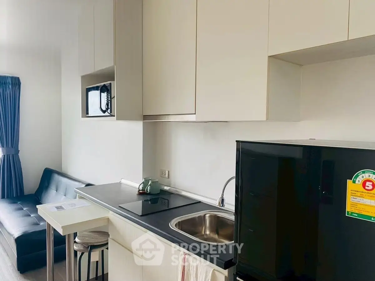 Modern compact kitchen with sleek black appliances and cozy living area in a stylish apartment.