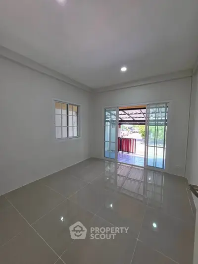 Spacious empty room with glossy tiled floor and large sliding glass doors leading to a covered patio.