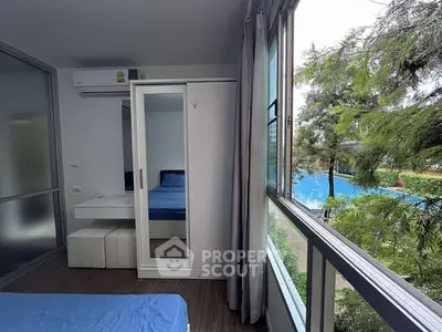 Modern bedroom with large window overlooking lush greenery and pool view.