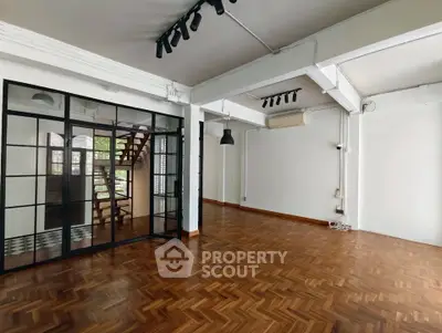 Spacious open-plan living area with parquet flooring and industrial-style glass partition.